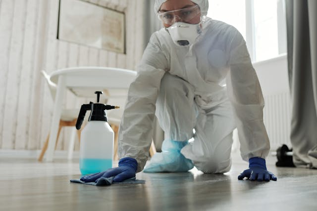 A Woman in White Coveralls Wiping a Floor while Wearing Gloves 